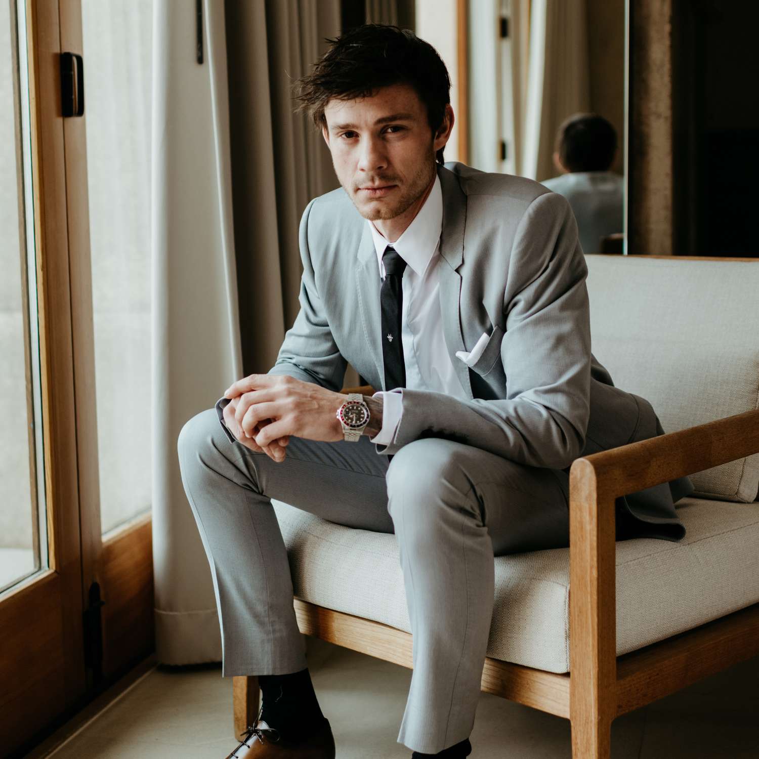 Person wearing a gray suit and black tie sitting on a chair