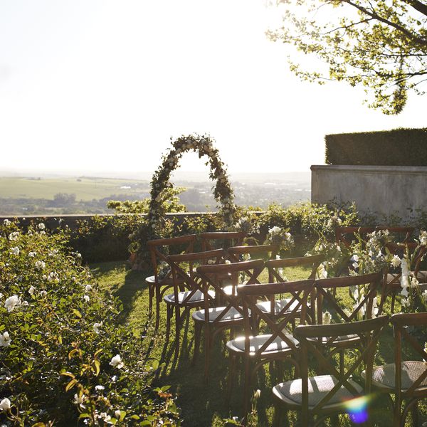 Wedding in Sunken Patio Garden With Green Bushes, Flower Arch, Wooden Chairs, and Rose Floral Arrangements