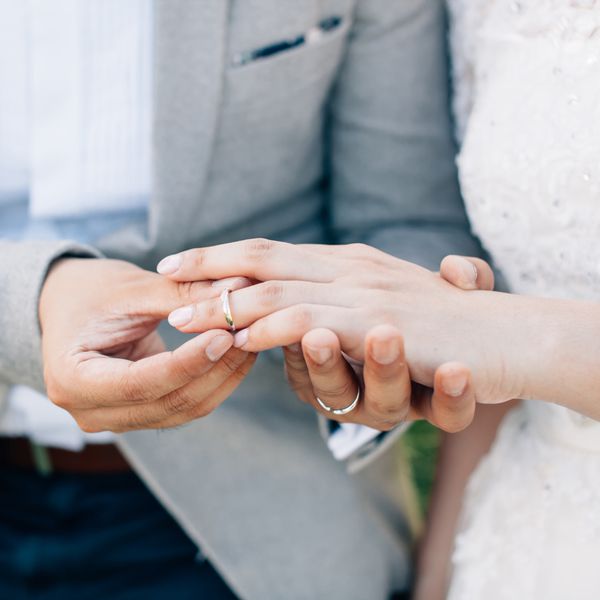 Closeup of Bride and Groomâs Hands As Groom Slips Gold Wedding Band on Brideâs Left Ring Finger