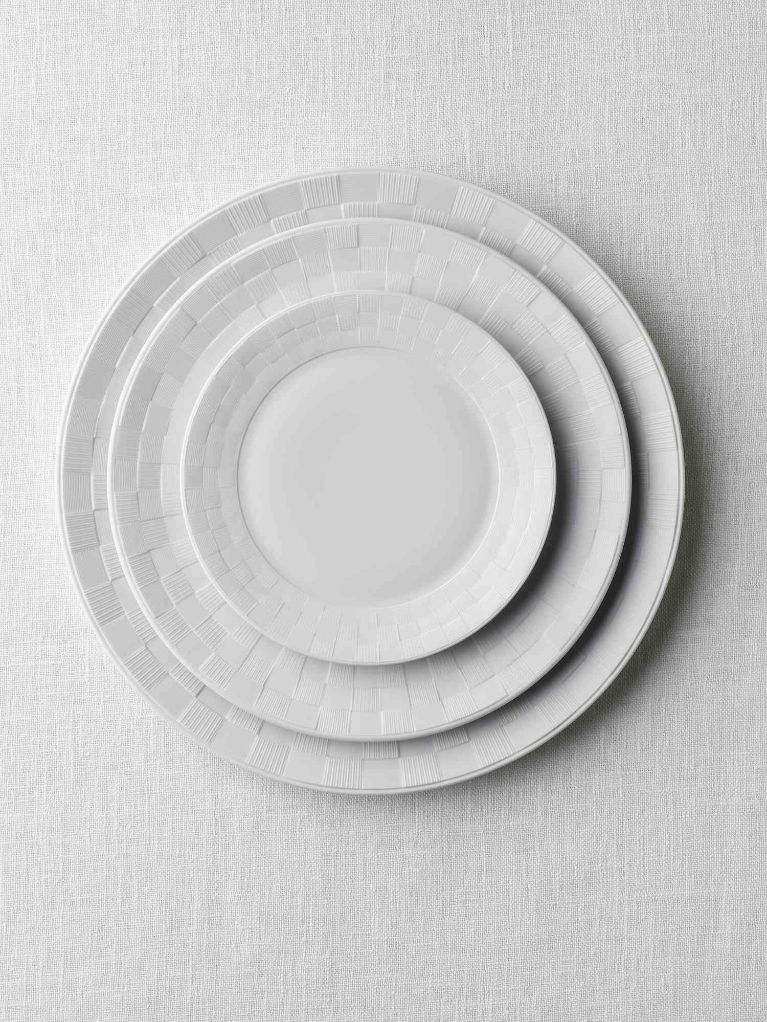 A stack of different sized ivory plates with a checkered pattern