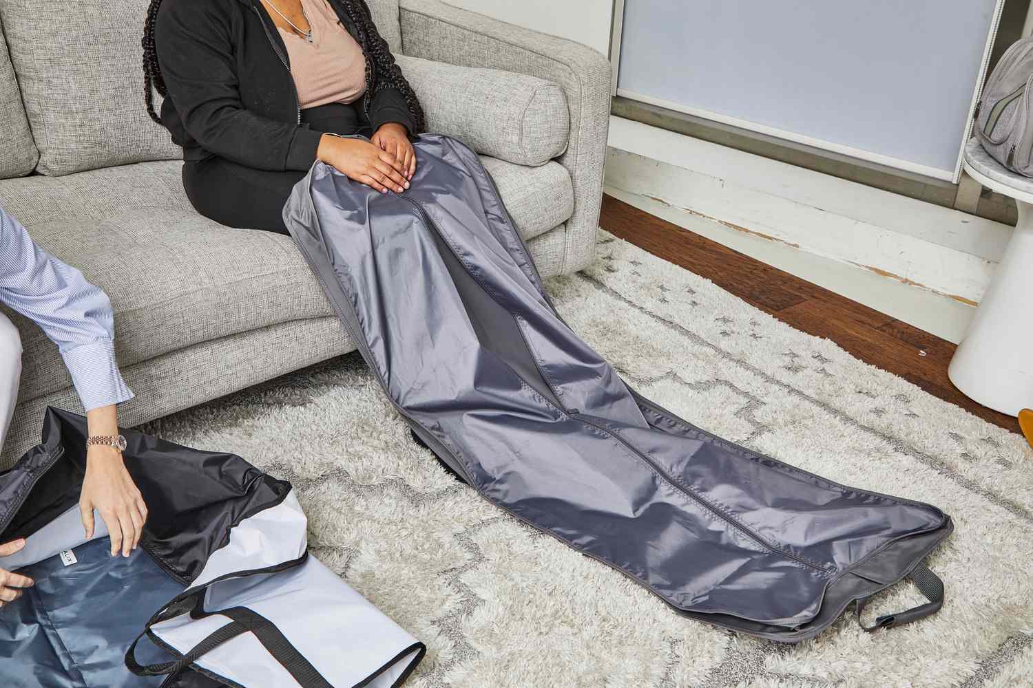 A person sitting on a sofa with the WallyBags Deluxe Garment Bag unzipped on their lap