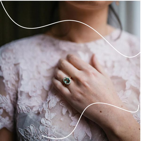 cluster design engagement ring with aquamarine center stone, diamond halo, and gold setting pictured against blush lace dress