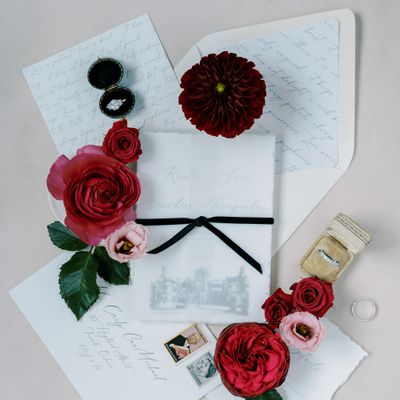 Wedding Invitation With Black Bow, Venue Illustration, and Deckled Edges Shown With Pink and Red Flowers