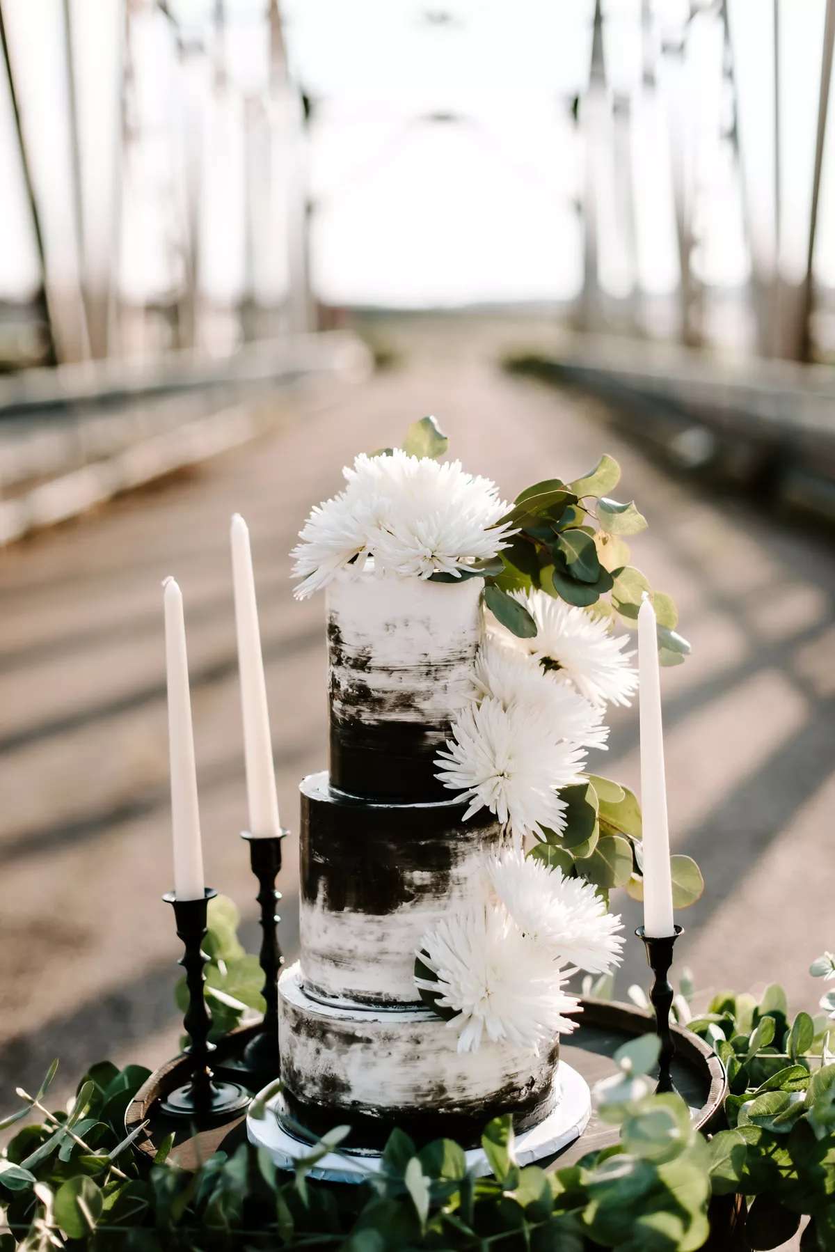 Black and white three-tier wedding cake with white florals and greenery next to candles