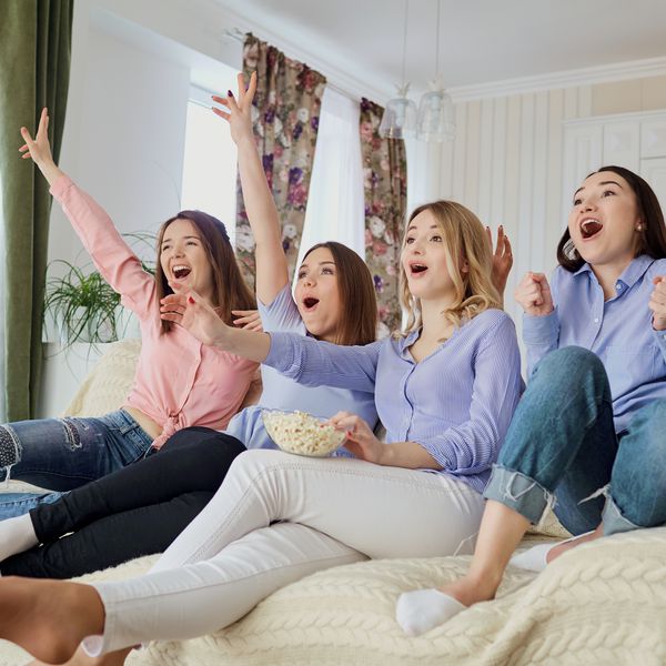 Four girlfriends sitting on a bed, eating popcorn and watching a movie