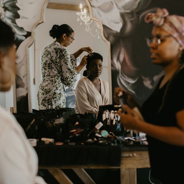 Bride with short hair looking in mirror while hair and makeup artists get her ready