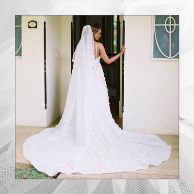 A bride smiling and wearing a white wedding dress with a long, lace wedding veil on her wedding day.