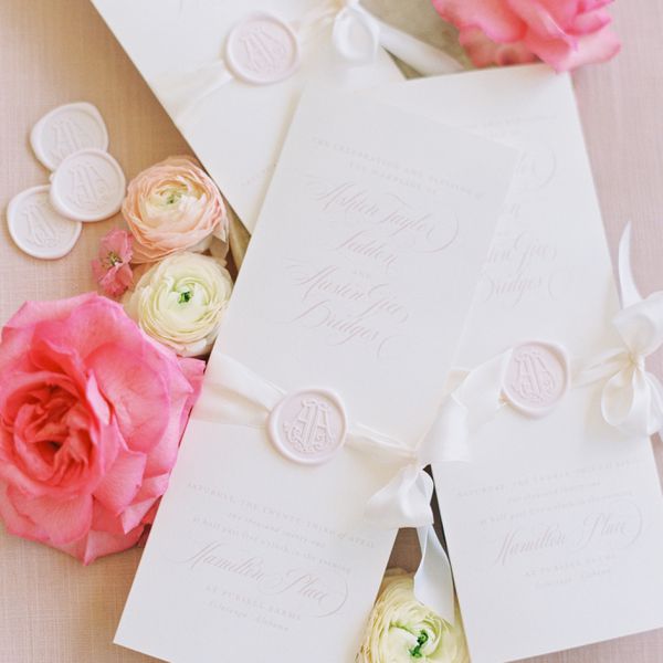 white wedding invitations with light pink font photographed with pink roses