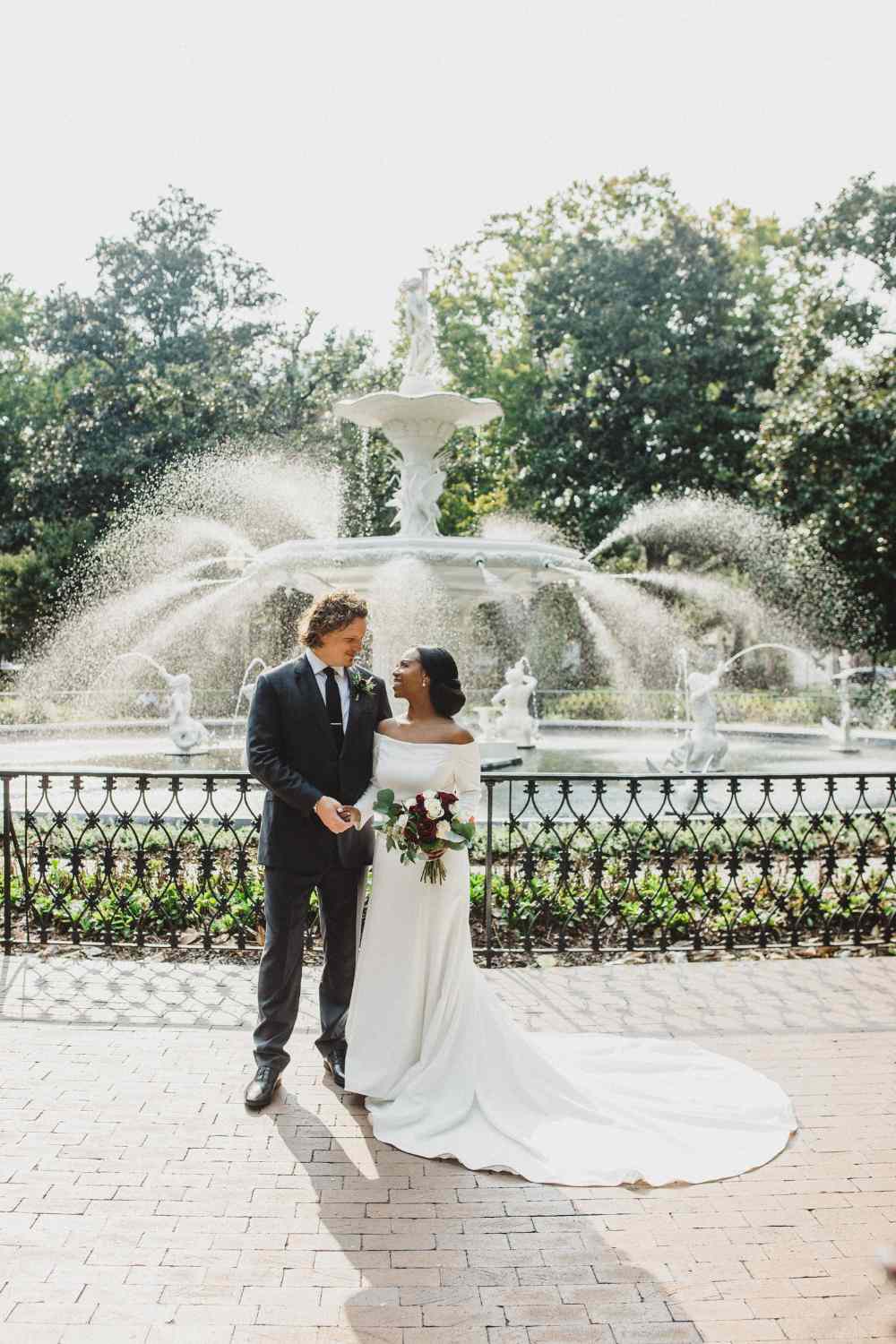 bride and groom posing in front of a water fountain for their wedding day portrait