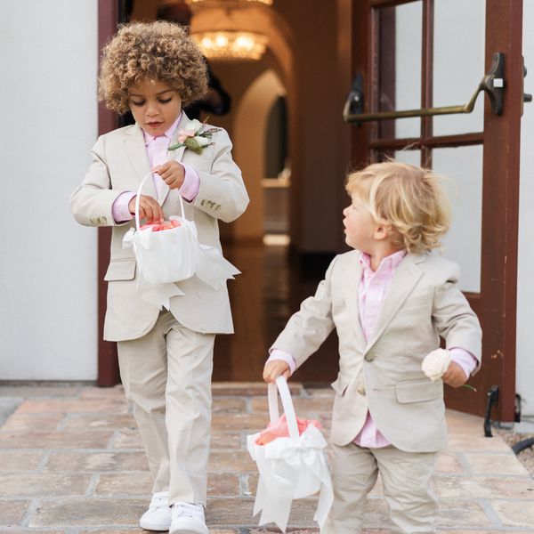 Two Boys Dressed in Tan Suits and Pink Shirts Holding White Baskets With Pink Petals