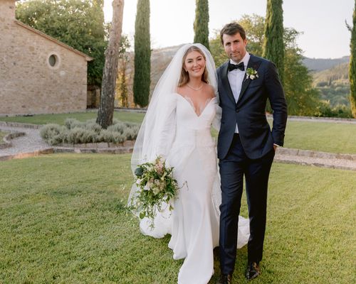 Bride in Wedding Dress and Veil Posing With Groom in Black Tuxedo in Garden