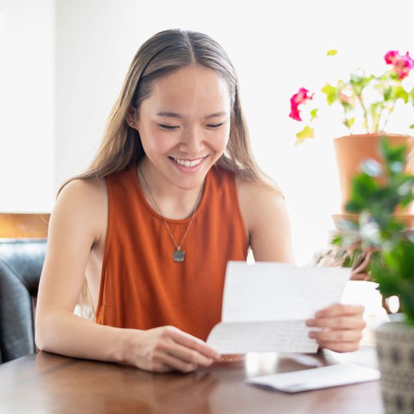 Brunette Woman Sitting Down at Table While Smiling and Looking at Invitation