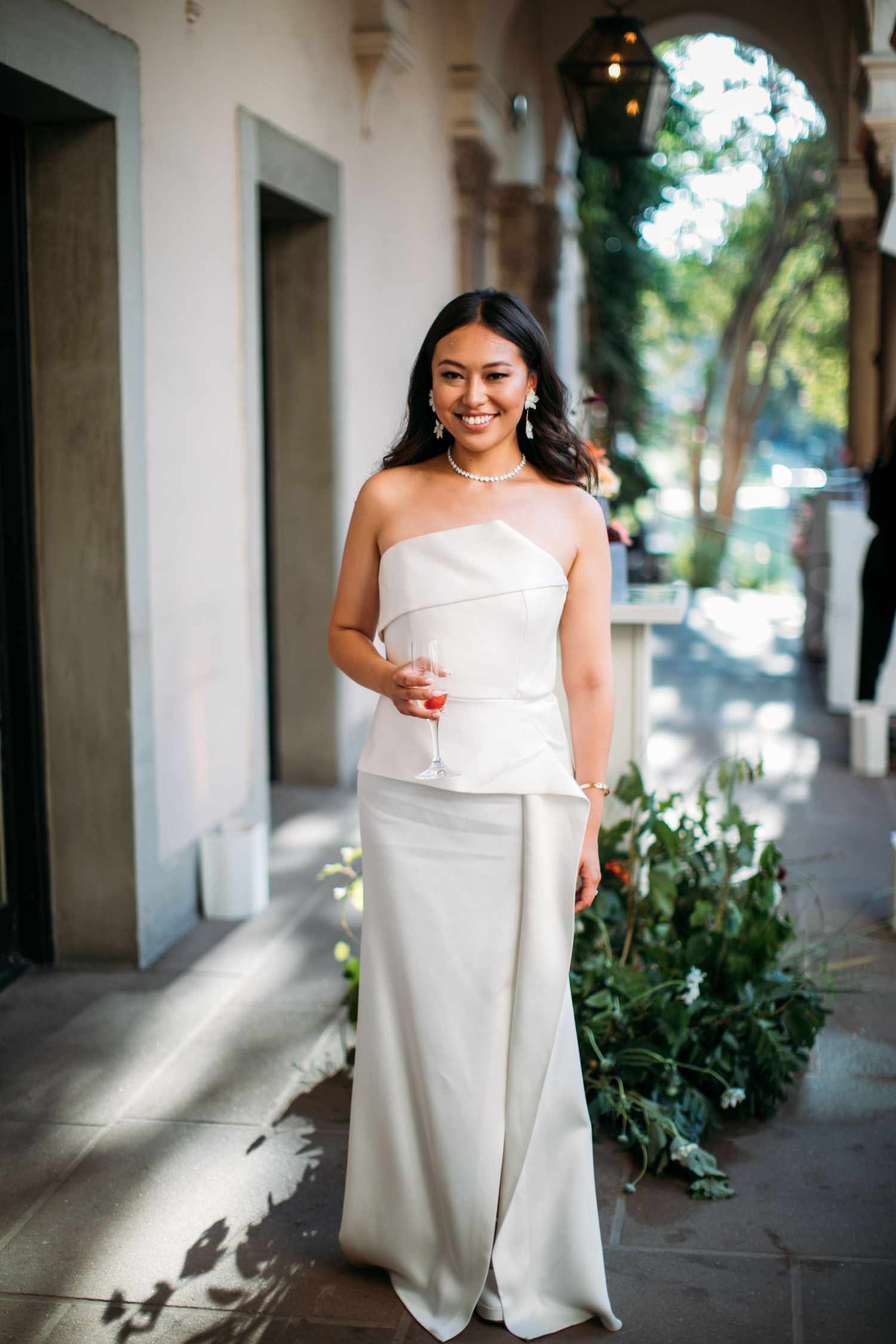 bride wearing a strapless column wedding dress holding a glass of champagne