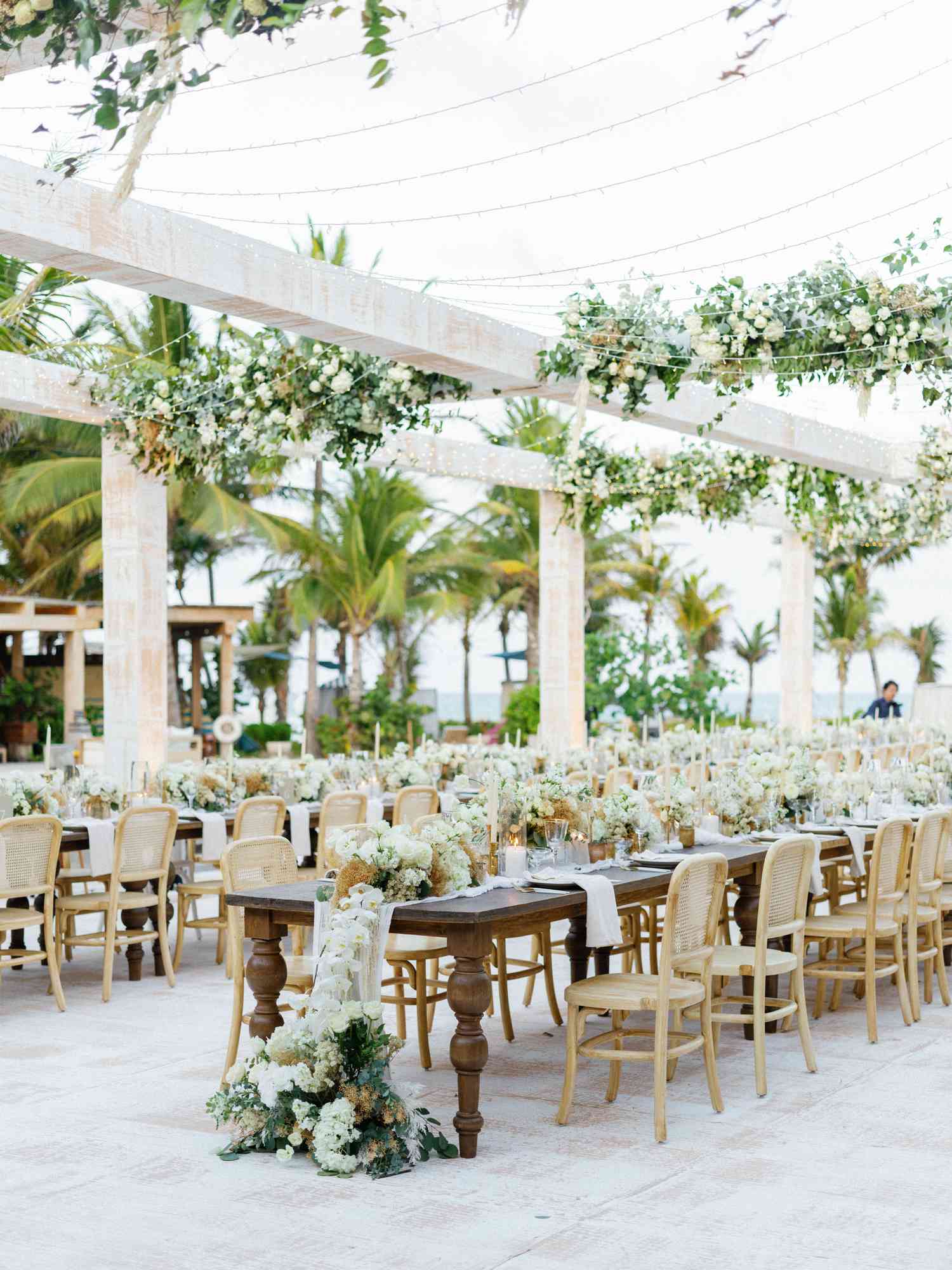 outdoor wedding reception with wooden tables, string lights, and white florals