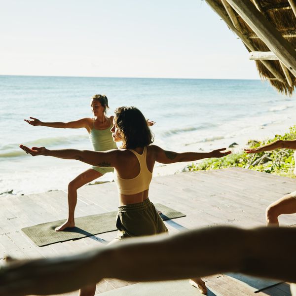 A group of women do yoga in an outdoor class at a hotel spa on the beach by the ocean.