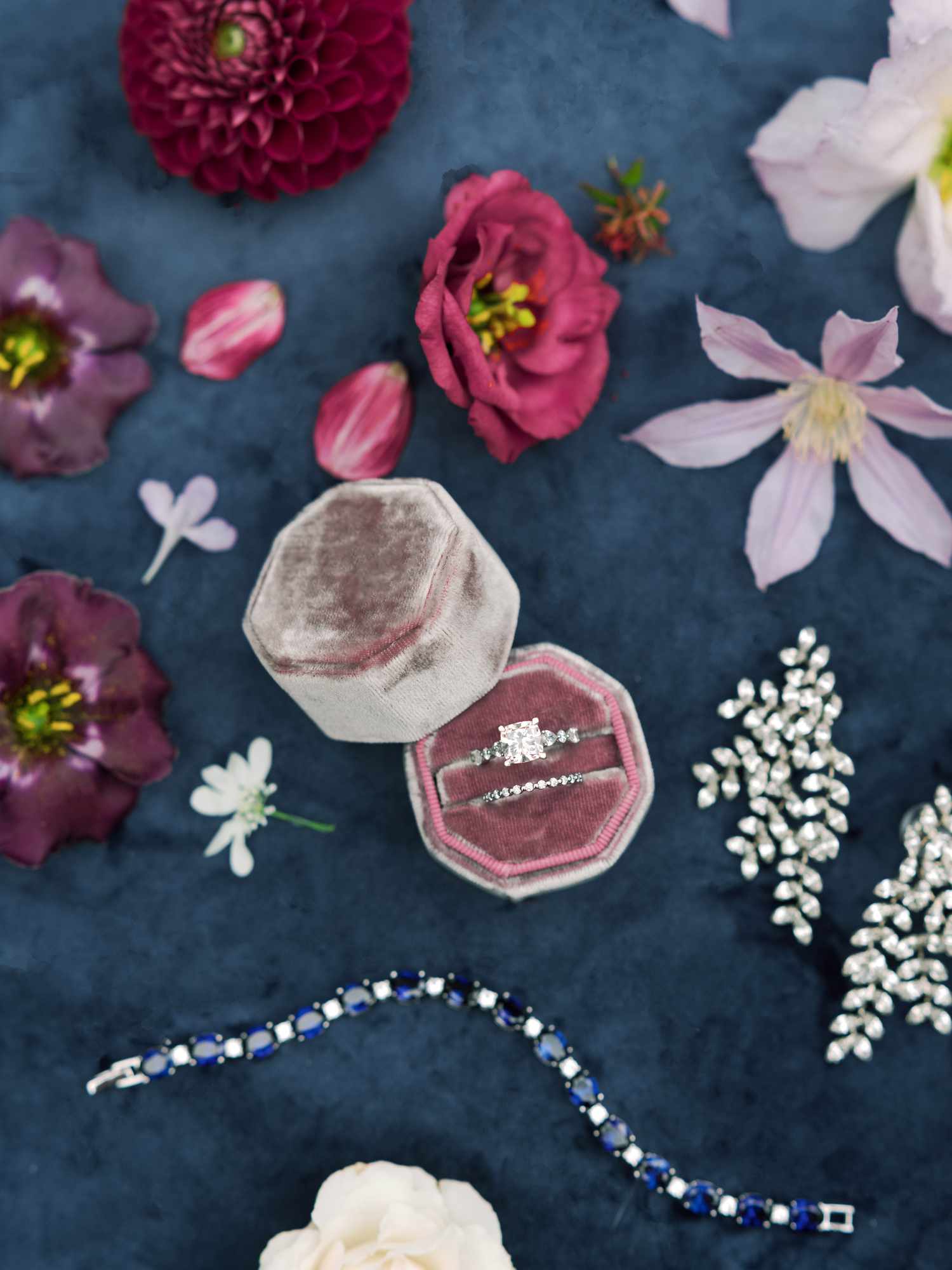 flat lay of engagement ring and wedding band in a ring box surrounded by pink and purple flowers 