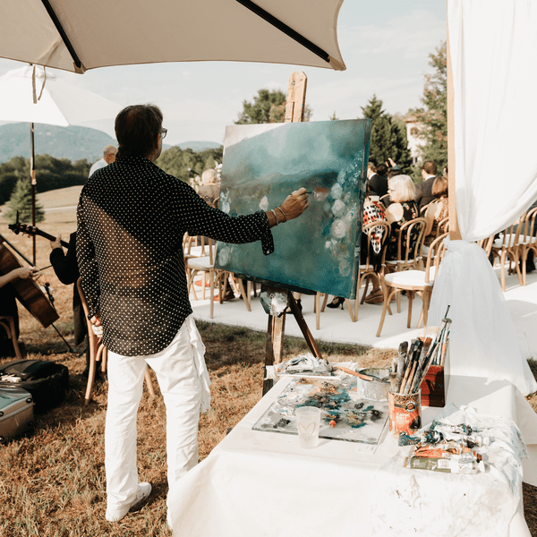 Artist completing live wedding painting of outdoor ceremony