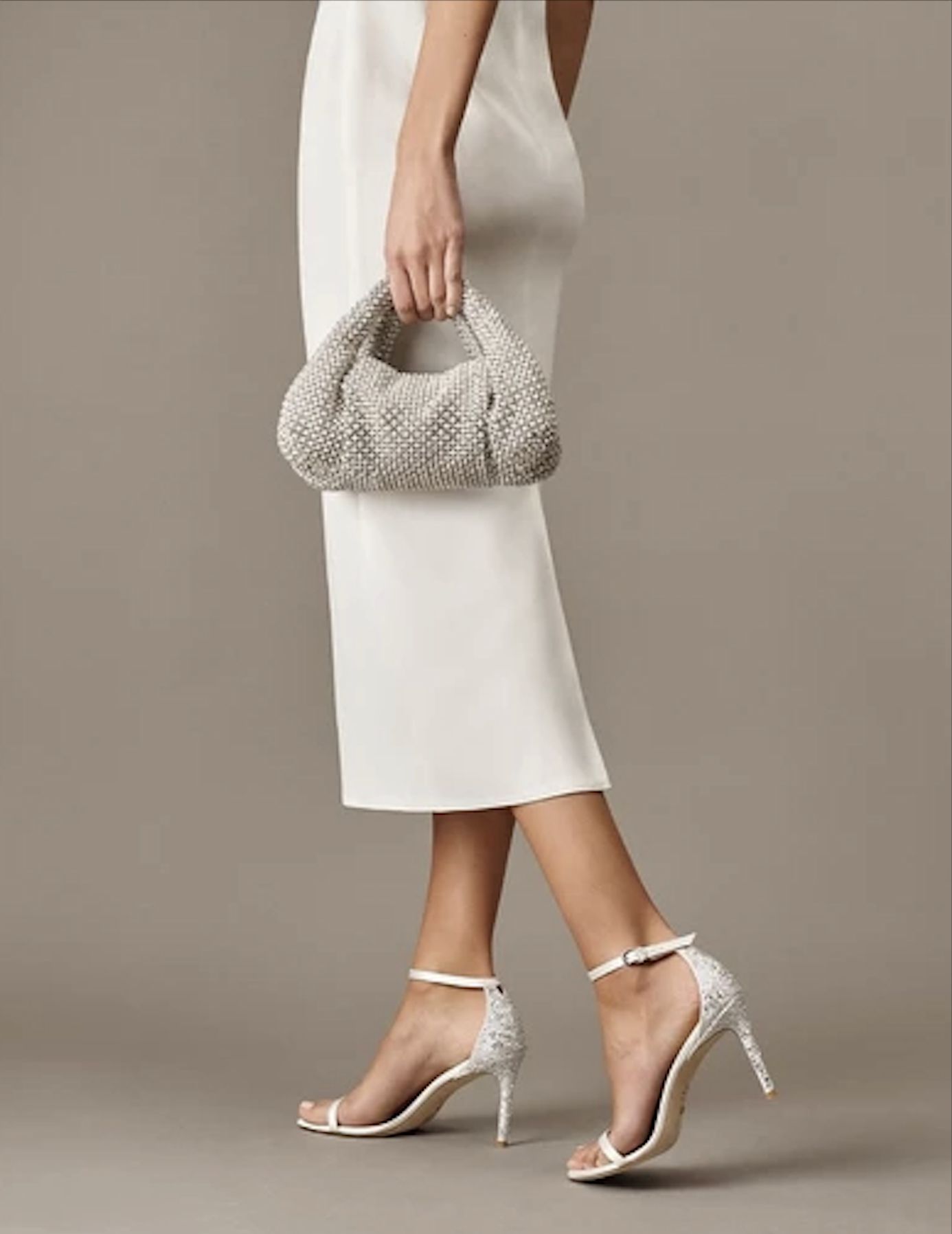 bottom half of a model wearing a white dress, white shoes, and silver mini bag