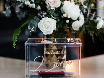 Acrylic Wedding Gift Box with Cards on White Table with White and Green Floral Arrangement Behind It