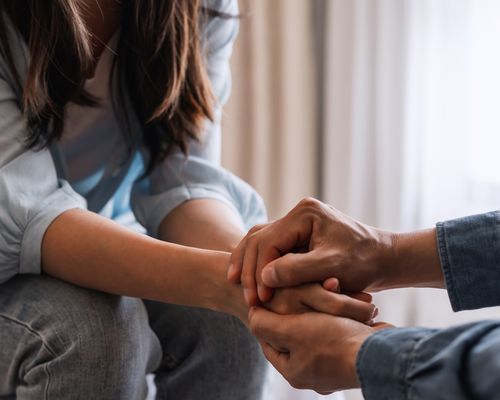 A husband sitting with his wife at home, holding hands and comforting her.