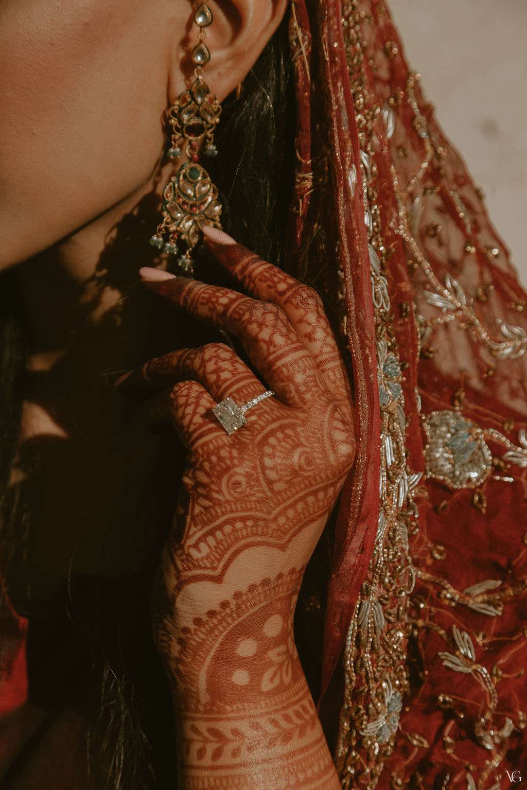 bride with henna on her hands touching her earrings to showcase her large cushion-cut engagement ring
