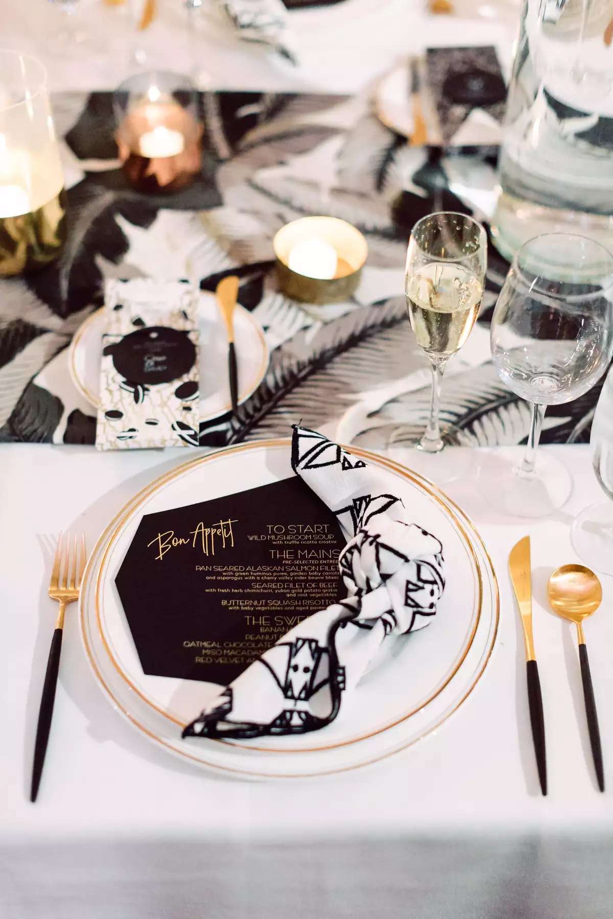 Wedding tablescape with patterned black and white napkin, black menu, and palm leaf print runner
