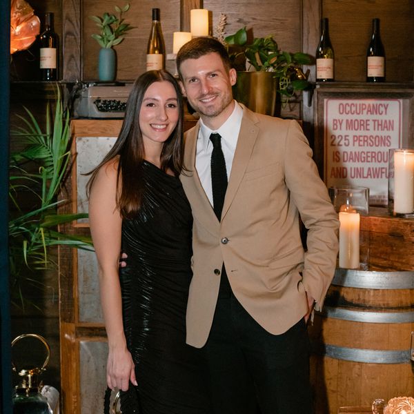 Dark-Haired Woman in Black Dress and Man in Tan Jacket Smiling