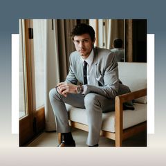 Person wearing a gray suit and black tie sitting on a chair