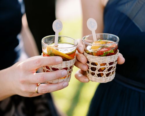 Signature wedding cocktails served in rattan cupholders at a wedding.