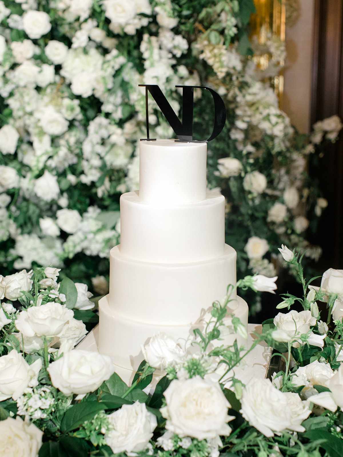 Four-tier white wedding cake with "ND" black topper and white flowers