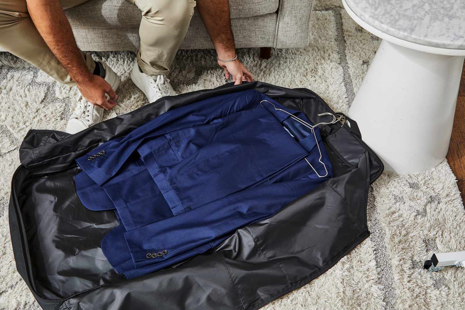 Zegur Suit Carry On Garment Bag laying on the floor while hands are reaching for the bag