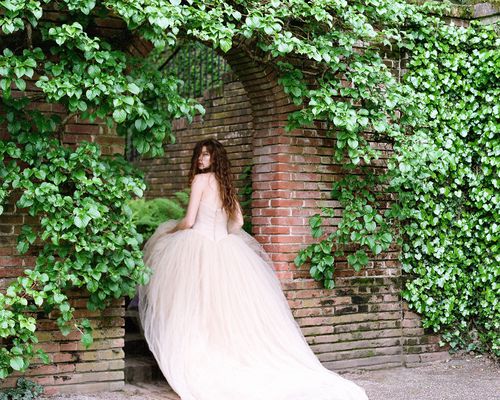 A balletcore bride wearing a tulle wedding dress walking into an ivy-covered venue in California.