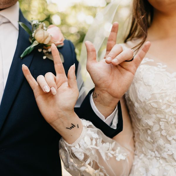 Closeup of Bride and Groomâs Interlocking Arms With Tattoo on Wrist and Hands Making âI Love Youâ Sign