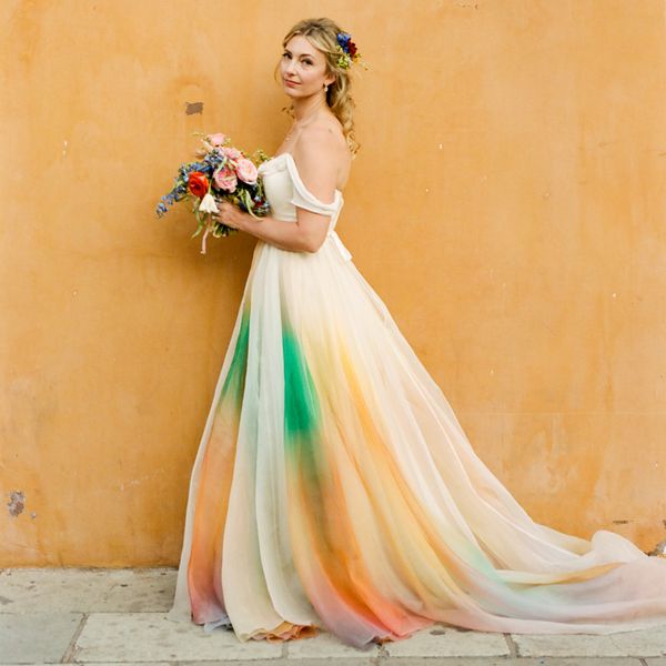 bride standing in front of an orange wall wearing a tie-dye wedding dress 