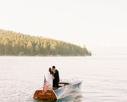 Bride and groom kissing on a boat with with an American flag on a lake