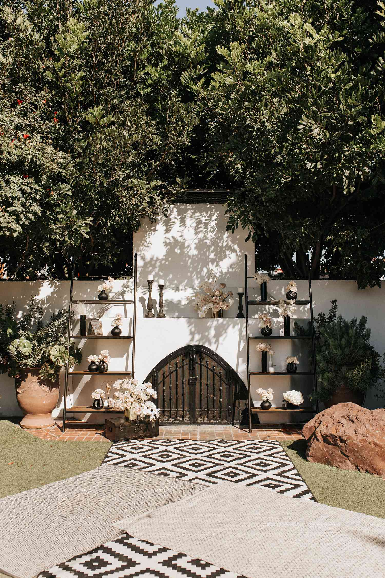 Black and white rugs on wedding ceremony aisle with altar with black vases and white florals