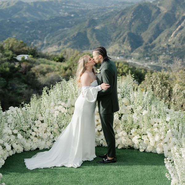 bride and groom kissing amongst a mountainous backdrop with white flowers surrounding them 