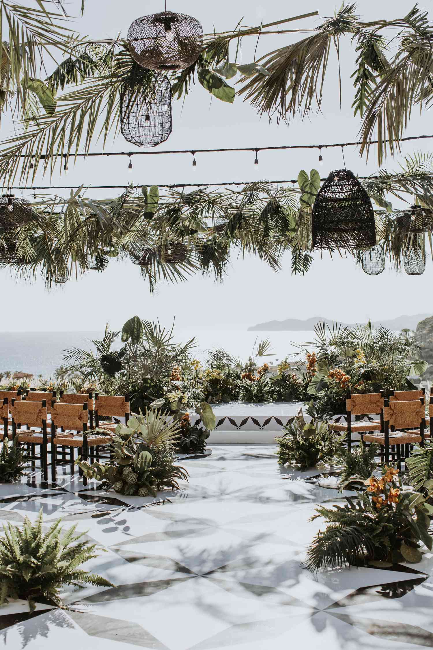 Ceremony Setting Decorated With Tropical Greenery and Black Rattan Lanterns Overlooking the Ocean
