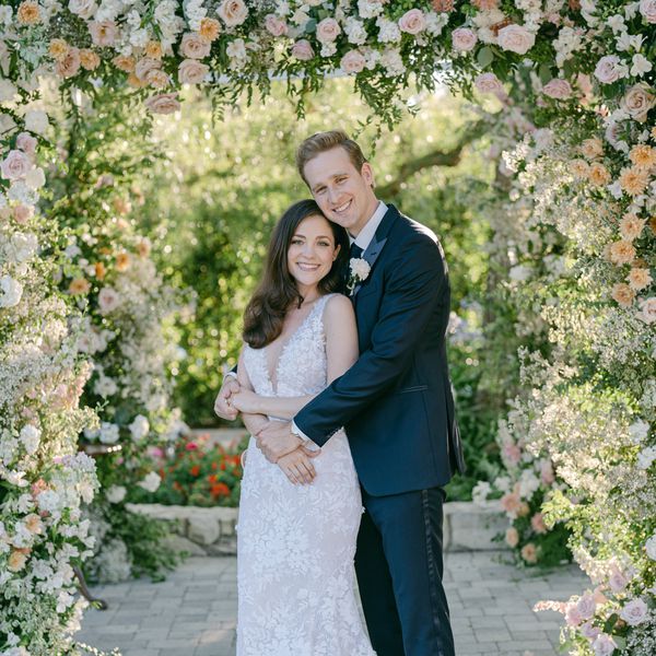 bride and groom posing for portrait against floral arch backdrop