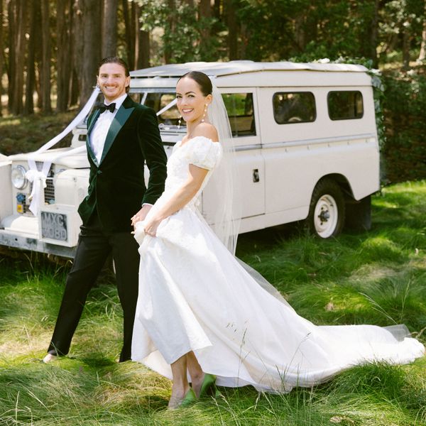 Bride in White Wedding Dress, Veil, And Pearl Earrings Posing With Groom in Dark Green Tuxedo in Front of Vintage White Van in The Woods 