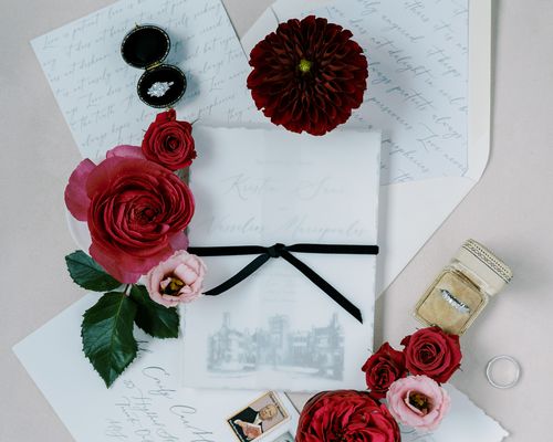 Wedding Invitation With Black Bow, Venue Illustration, and Deckled Edges Shown With Pink and Red Flowers