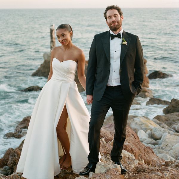 Bride in Strapless Wedding Dress and Groom in Black Tuxedo Posing on a Rock in Front of the Ocean