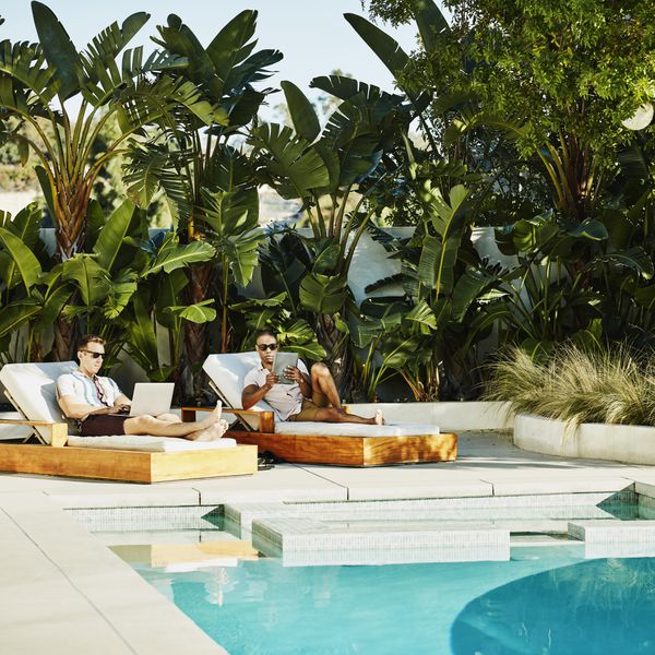 two men sit by a pool surrounded by palm trees on their honeymoon