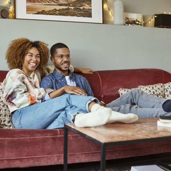 A young black couple sitting together and watching tv on a red couch