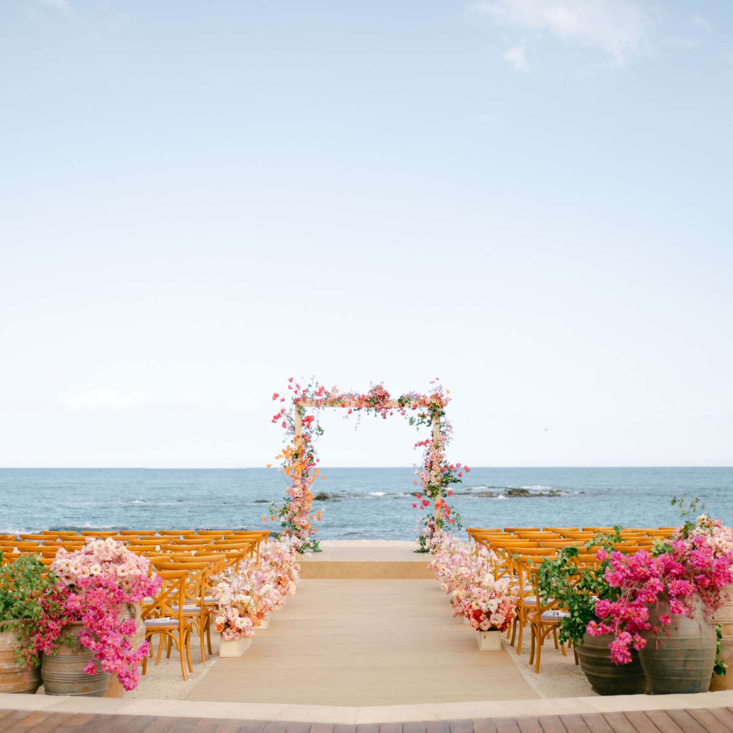 Ceremony Setup With Hot Pink Flowers Marking the Beginning and Perimeter of the Aisle and a Floral Arch Overlooking the Ocean
