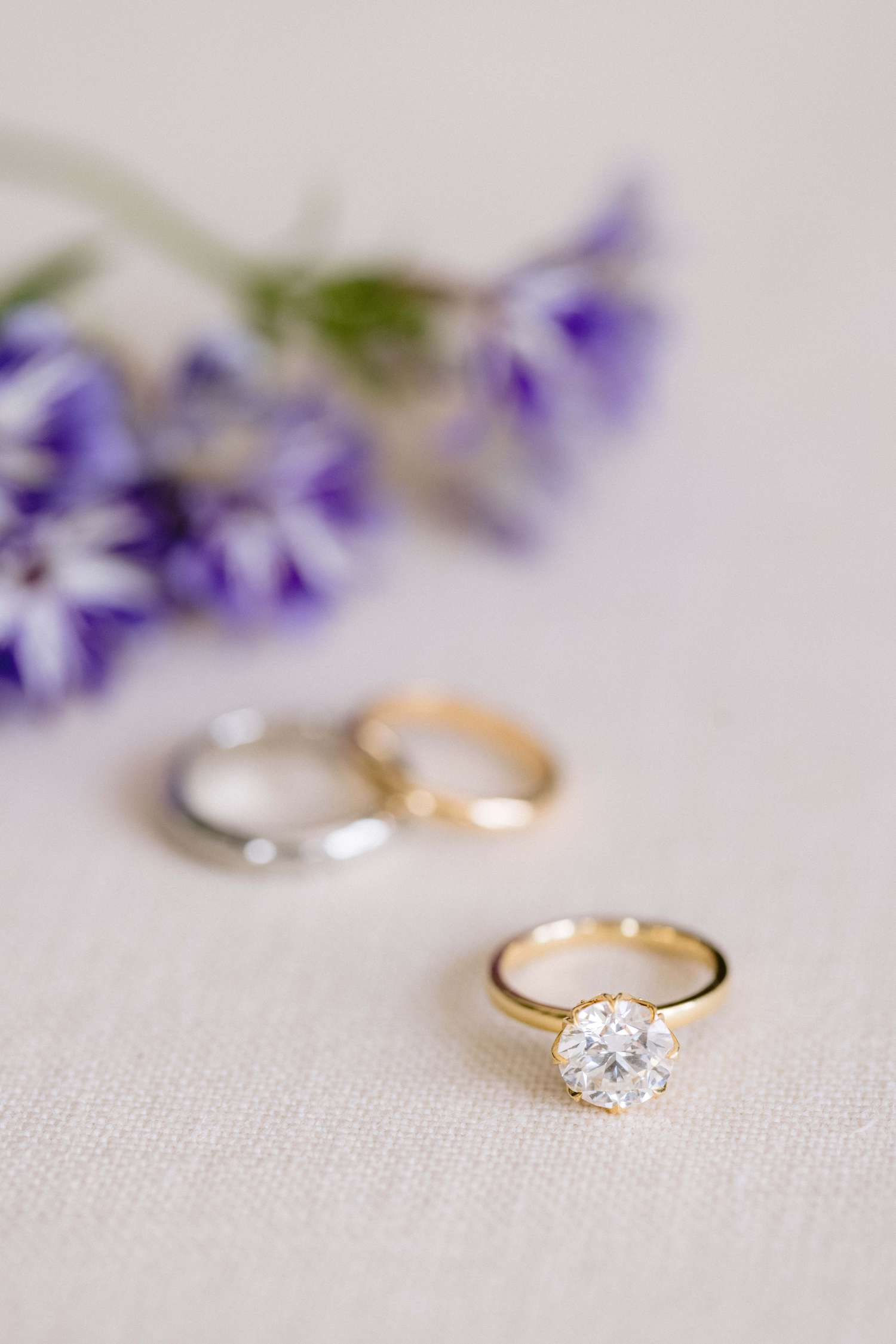 still shot of diamond engagement ring with a purple flowers slightly blurred in the background