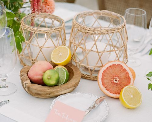 tablescape with citrusâgrapefruit, lemons, limes, and a peachâand white candles in a wicker-like vase 