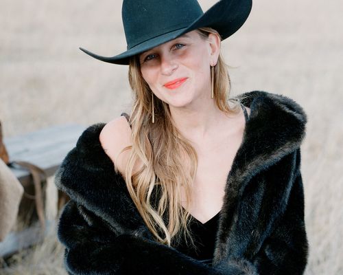 a wedding guest wearing a black cowboy hat and a black fur coat