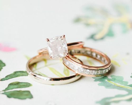 Cushion-cut engagement ring on rose gold band beside two wedding bands