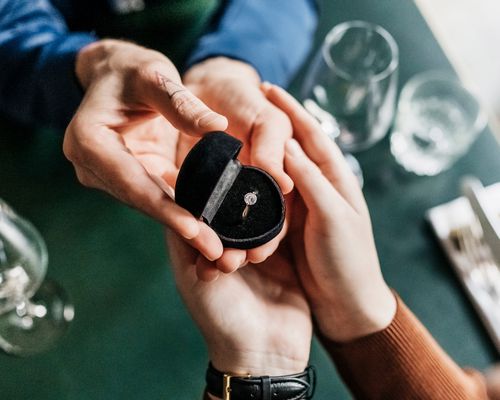 man giving woman engagement ring in box at dinner table